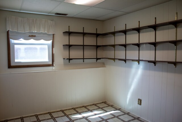 empty room featuring wainscoting, tile patterned floors, visible vents, and a drop ceiling