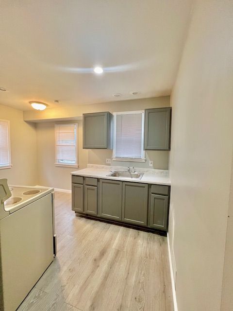 19676 Kingsville St, Harper Woods, MI 48225 - kitchen with gray cabinets, a sink, light wood-type flooring, baseboards, and range