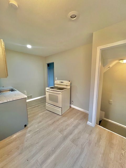 19676 Kingsville St, Harper Woods, MI 48225 - kitchen featuring white electric stove, light countertops, a sink, light wood-style floors, and baseboards