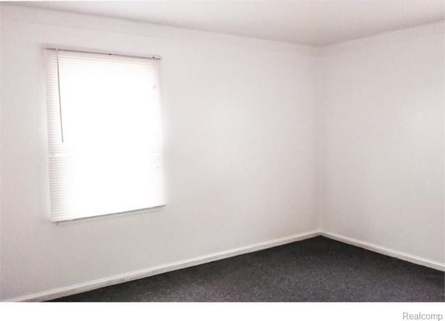 empty room featuring dark colored carpet and baseboards