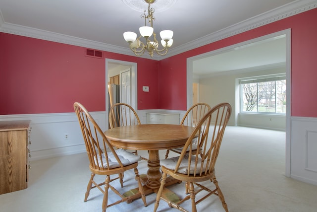 dining room with a wainscoted wall, carpet flooring, visible vents, a chandelier, and ornamental molding