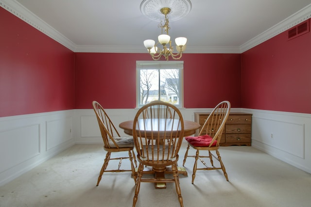 carpeted dining space featuring wainscoting, visible vents, an inviting chandelier, and ornamental molding