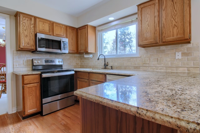 kitchen featuring backsplash, appliances with stainless steel finishes, a sink, and light wood-type flooring