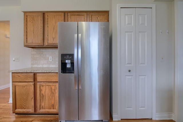 kitchen featuring tasteful backsplash, light stone counters, stainless steel fridge, light wood-style flooring, and baseboards