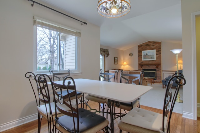 dining area featuring wood finished floors, a brick fireplace, lofted ceiling, and a wealth of natural light