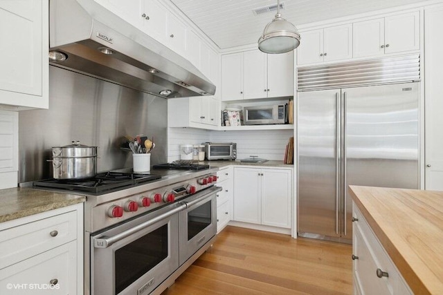 kitchen featuring white cabinets, visible vents, butcher block countertops, high end appliances, and under cabinet range hood
