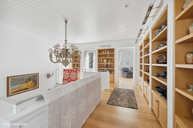 hallway featuring built in features, a chandelier, and light wood finished floors