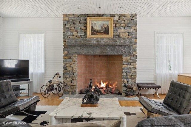 living area featuring wooden ceiling, a stone fireplace, and wood finished floors