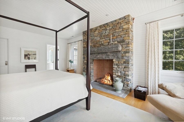 bedroom with a stone fireplace, wood finished floors, and multiple windows