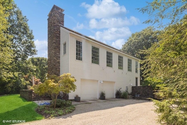 exterior space featuring an attached garage, driveway, a chimney, and cooling unit