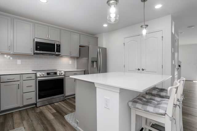 kitchen featuring gray cabinets, a kitchen bar, dark wood-style flooring, appliances with stainless steel finishes, and tasteful backsplash