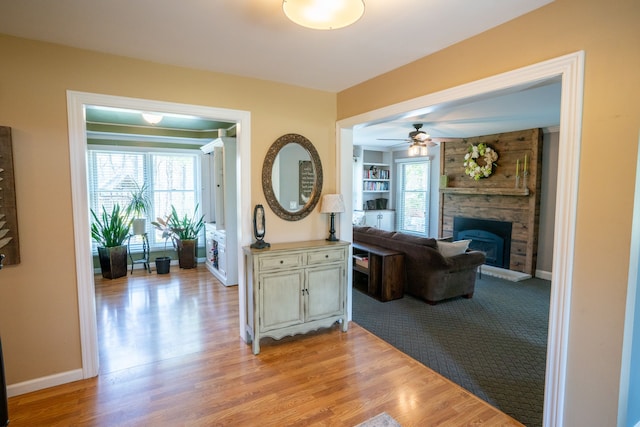 hallway featuring baseboards, built in shelves, and light wood-style floors