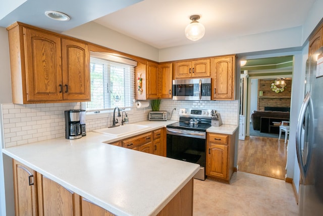 kitchen featuring brown cabinetry, appliances with stainless steel finishes, light countertops, a sink, and a peninsula