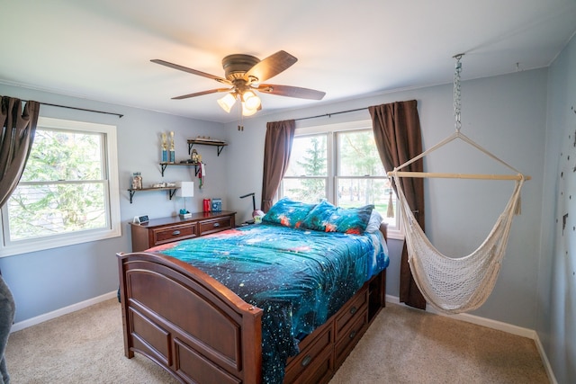 bedroom with ceiling fan, light carpet, baseboards, and multiple windows