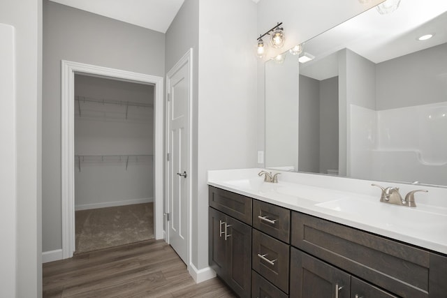 full bath with a walk in closet, double vanity, wood finished floors, and a sink