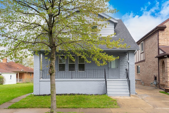 bungalow with brick siding, a front lawn, roof with shingles, and covered porch