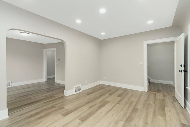 empty room featuring arched walkways, baseboards, light wood finished floors, and visible vents