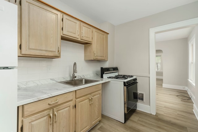 kitchen with light wood-type flooring, gas stove, a sink, freestanding refrigerator, and light brown cabinets