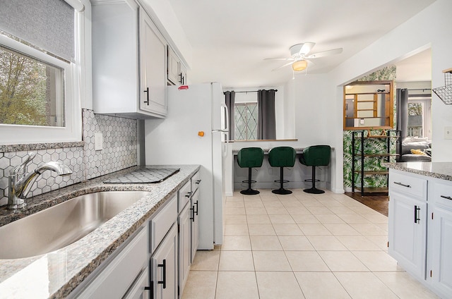 kitchen with ceiling fan, light stone countertops, a sink, decorative backsplash, and light tile patterned floors