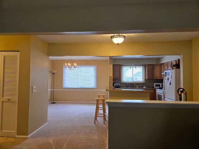 kitchen with an inviting chandelier, light carpet, a sink, and white appliances