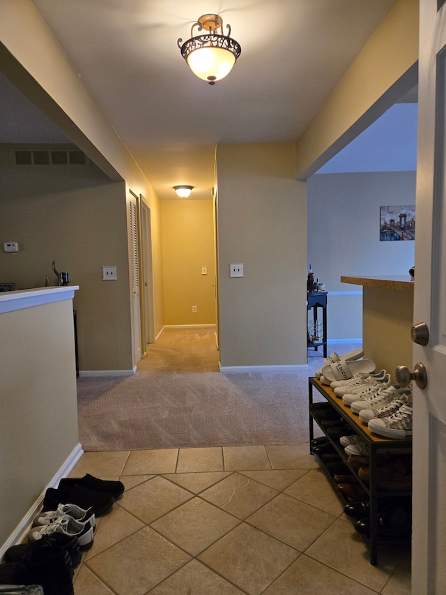hallway featuring carpet flooring, visible vents, tile patterned flooring, and baseboards