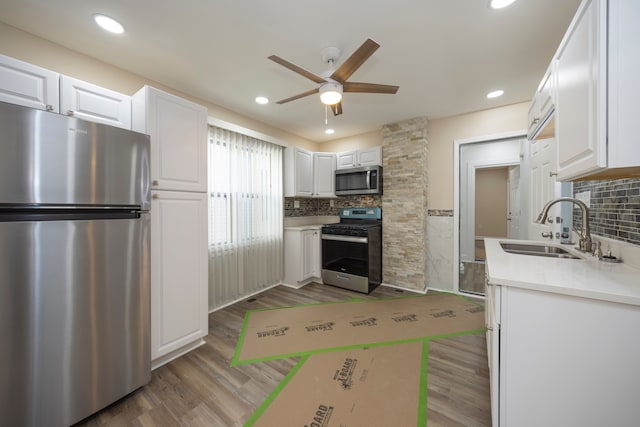 kitchen featuring wood finished floors, appliances with stainless steel finishes, white cabinets, a sink, and a ceiling fan