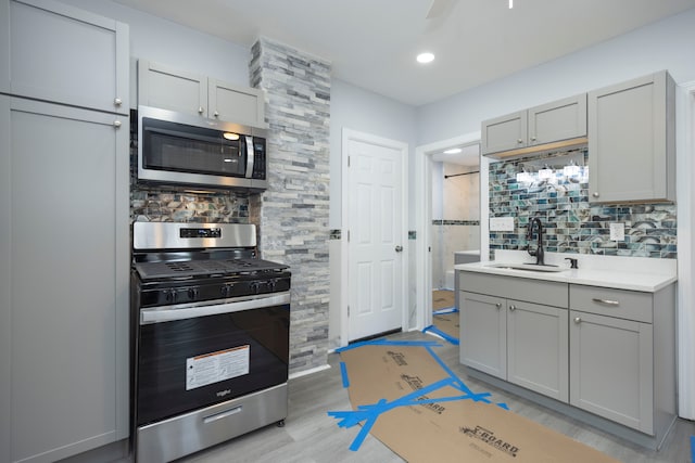 kitchen with a sink, stainless steel appliances, gray cabinets, light wood-type flooring, and backsplash
