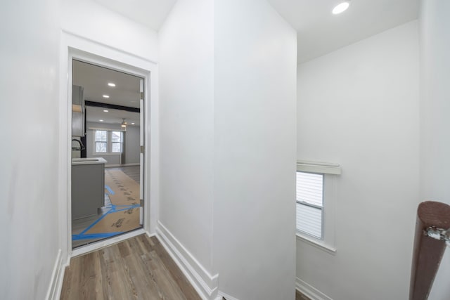 corridor featuring a sink, wood finished floors, recessed lighting, and baseboards