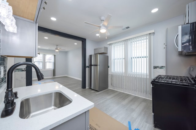 kitchen with a sink, ceiling fan, visible vents, black range with gas cooktop, and freestanding refrigerator