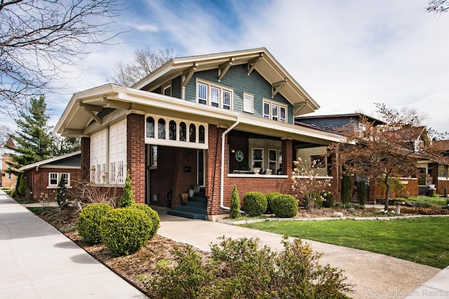 view of front of house with covered porch, a front lawn, and brick siding