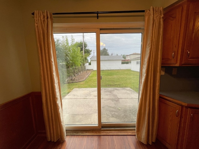 doorway with wood finished floors and a wainscoted wall