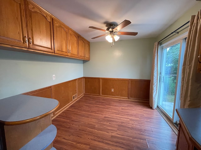unfurnished dining area with a ceiling fan, dark wood finished floors, wainscoting, and a healthy amount of sunlight