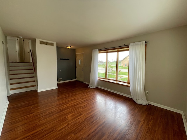 unfurnished living room with visible vents, baseboards, dark wood-style flooring, and stairs