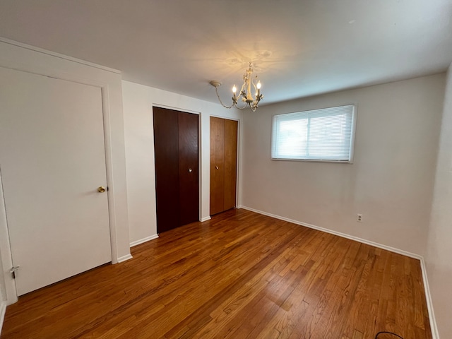 unfurnished bedroom featuring multiple closets, baseboards, wood finished floors, and a chandelier