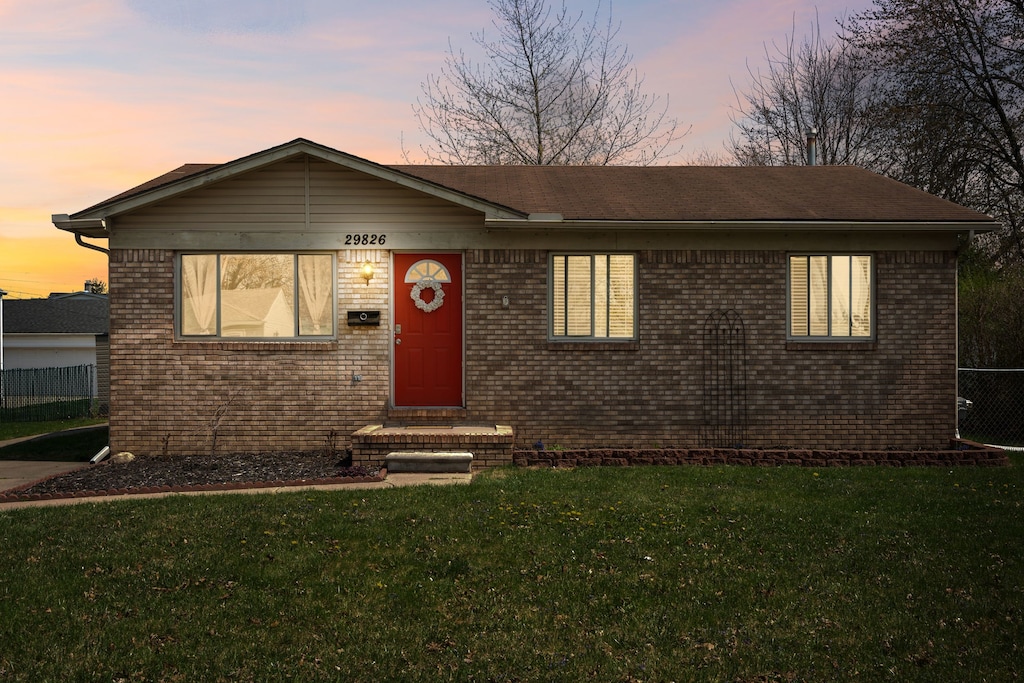 ranch-style home featuring fence, a front lawn, and brick siding