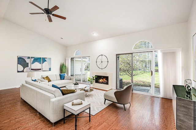 living room featuring wood finished floors, visible vents, a ceiling fan, a lit fireplace, and high vaulted ceiling