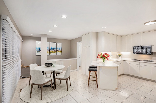 kitchen with white cooktop, black microwave, a breakfast bar, light countertops, and a peninsula