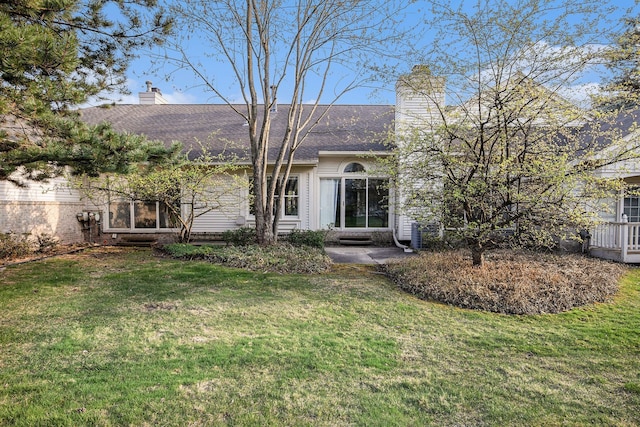 back of property with a chimney, a shingled roof, and a yard