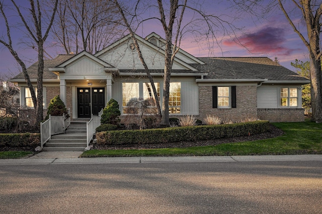 view of front of property with a lawn, roof with shingles, and brick siding