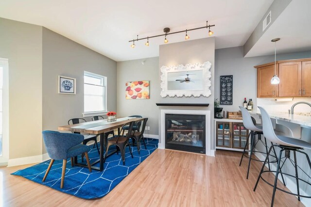 dining room with baseboards, a glass covered fireplace, visible vents, a ceiling fan, and wood finished floors