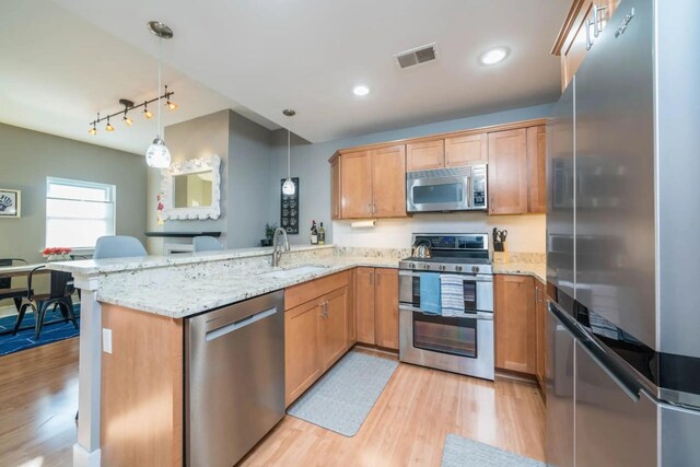 kitchen featuring stainless steel appliances, visible vents, light wood-style floors, decorative light fixtures, and a peninsula