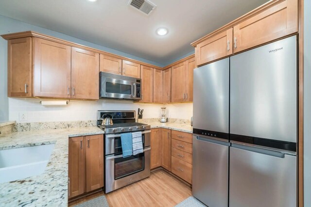 kitchen with light stone counters, visible vents, light wood finished floors, and stainless steel appliances