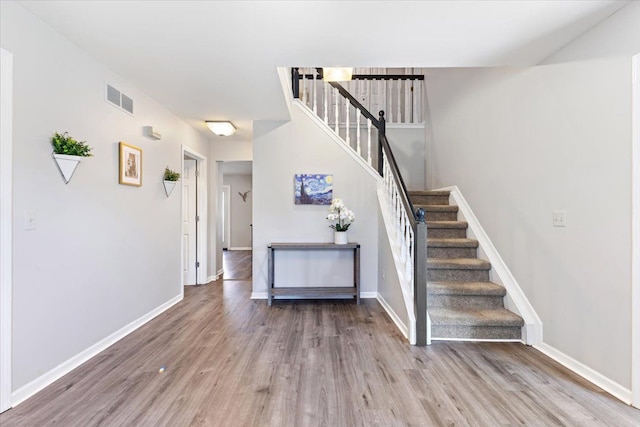 stairway with wood finished floors, visible vents, and baseboards