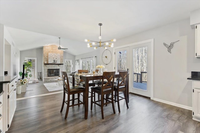 dining area featuring vaulted ceiling, dark wood-type flooring, baseboards, a brick fireplace, and a notable chandelier