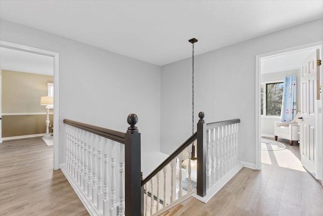hall featuring light wood-type flooring, baseboards, and an upstairs landing