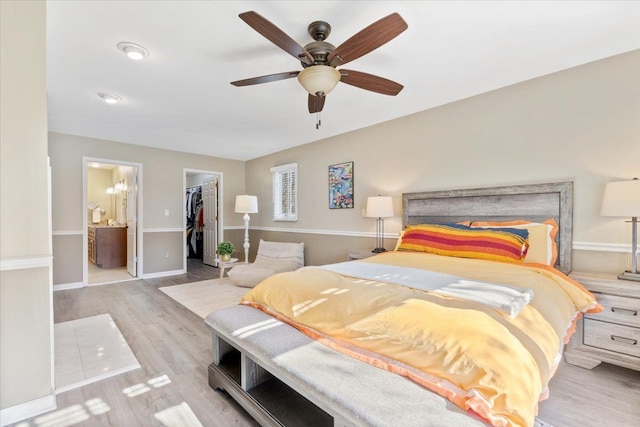 bedroom with wood finished floors, a walk in closet, a closet, ensuite bath, and baseboards