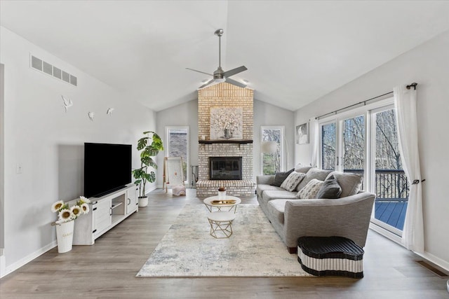 living room featuring wood finished floors, ceiling fan, a fireplace, lofted ceiling, and visible vents