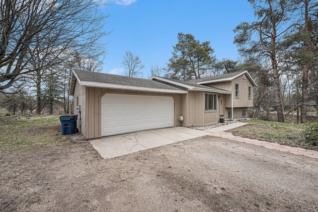 split level home with an attached garage, driveway, and a shingled roof