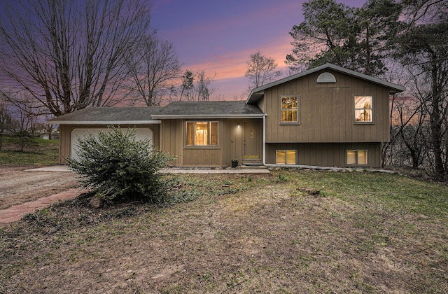 tri-level home featuring a garage, dirt driveway, and a shingled roof