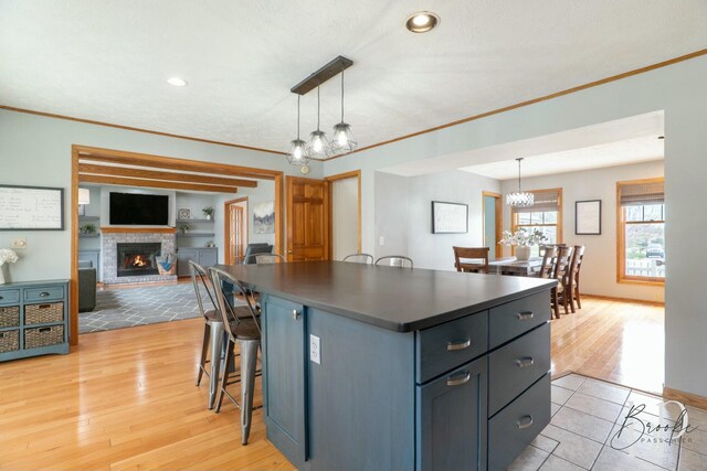 kitchen with dark countertops, a chandelier, a lit fireplace, ornamental molding, and a kitchen island
